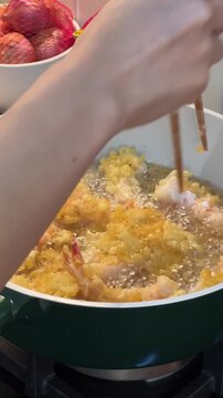 Passionate asian female influencer and home cook prepares food to deep fry delicious shrimp tempura in hot oil using green pot recording joyful culinary vlog with smartphone sharing emotion
