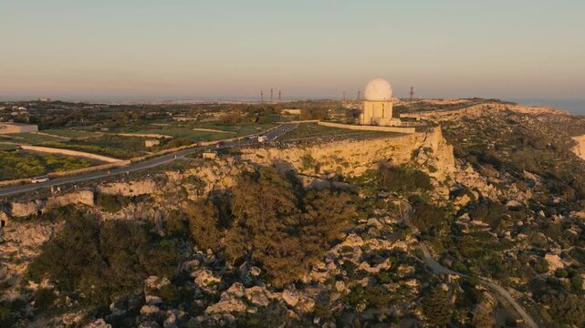 Aerial drone orbit over Dingli cliffs, Malta with sunset viewpoint crowd, coastal escarpment and historic radar structure on southwest coastline. a popular sunset viewing location along the island