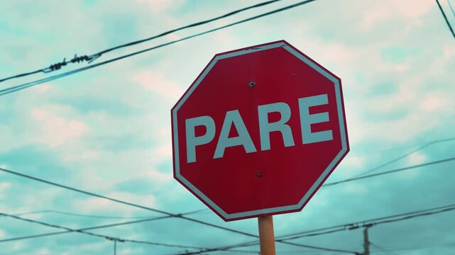 Red PARE stop sign under a dramatic cloudy sky with power lines