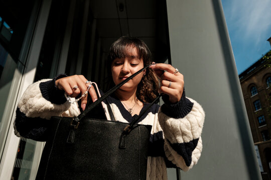 Young woman searching everyday handbag for items on street