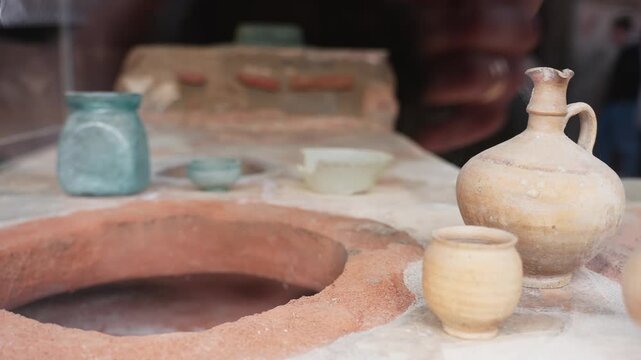 Ancient Roman pottery displayed inside a Pompeii thermopolium, with ceramic jugs, small cup, dolia opening, and soft museum-style interior light.