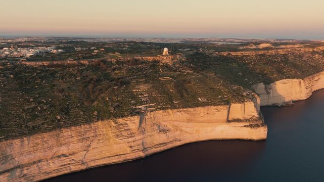 Aerial drone approach to Dingli Cliffs sunset viewpoint in Malta with golden limestone rocks, sea horizon and visitors watching sunset. Dingli Cliffs sunset viewpoint in Malta during golden hour