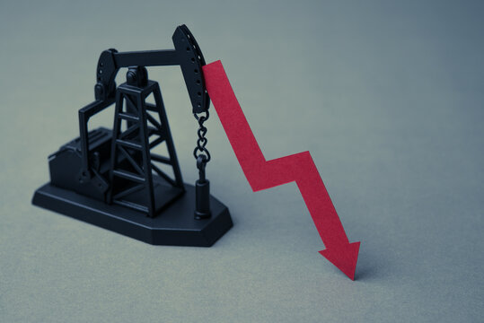 Crude oil pumpjack with red falling prices chart on grey background copy space. Oil price down in commodity trading market due to recession economy, global low demand, US shale oil reserves concept.
