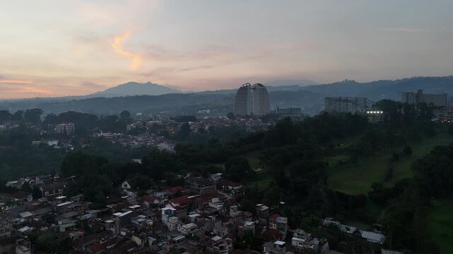 Drone aerial view of Bandung in the evening, surrounded by rolling hills and warm sunset light, showcasing the beauty of the city and nature.