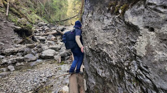 Man clad in hiking gear skillfully navigates a log as he makes his way along a narrow trail in the breathtaking landscape of Sucha Bela canyon within Slovak Paradise National Park