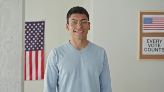 Man smiling with american flag and voting poster in a polling building; civic pride voter participation.