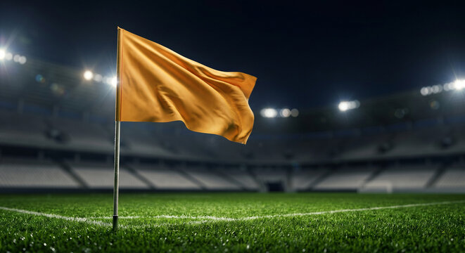 Close up of a blank orange corner flag on a stadium soccer field at night