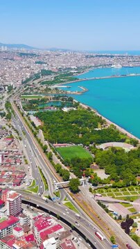 Vertical video. Samsun, Turkey. Aerial panorama of the Black Sea coastline, dense terracotta rooftops and coastal highway stretching toward the harbor under clear summer skies. Aerial View. Rich colo
