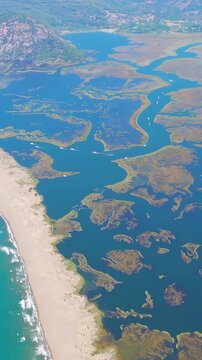 Vertical video. Dalyan, Turkey. Iztuzu Turtle Beach, a 4.5km golden sand spit where the Dalyan River meets the Mediterranean Sea, aerial drone view showing winding delta channels and turquoise waves.