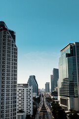 Fototapeta premium ertical mobile-friendly cityscape of Bangkok featuring modern skyscrapers, luxury condominiums, office towers, and elevated railway system under bright blue sky. Contemporary urban architecture and me