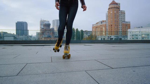 Low angle view of female legs in yellow vintage roller skates performing tricks on city square tiles.