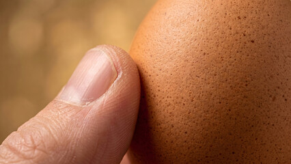 Fototapeta premium Extreme Macro Shot of a Human Thumb Pressing Against a Speckled Brown Eggshell