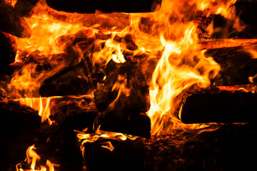 Fototapeta premium Narrow focus of a crackling bonfire at night in Brazil. Orange flames dance among stacked wood, illuminating the darkness. Sparks fly up, creating a fascinating visual spectacle.