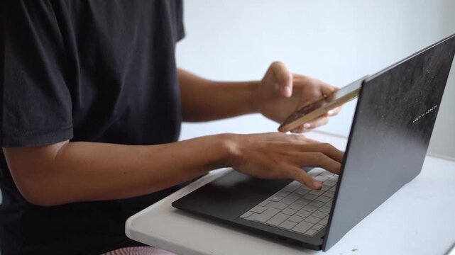 Close Up View of Man Hands Multi-Tasking Typing on Laptop Keyboard While Holding and Checking Smartphone