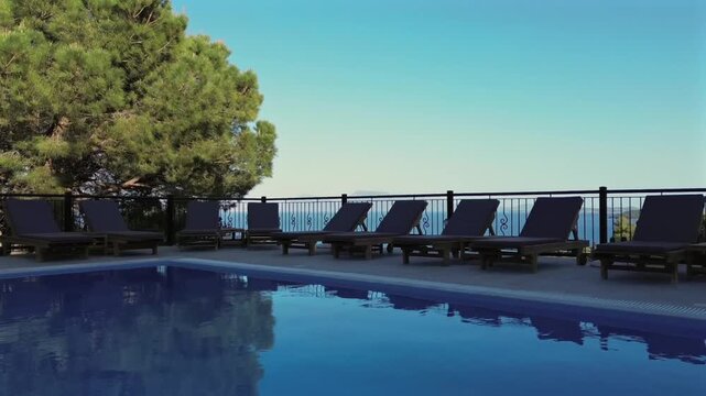 Aerial drone smooth shot flying over a blue swimming pool and sunbeds to reveal a scenic view of the Ionian Sea in Greece. High quality 4K luxury travel stock video.