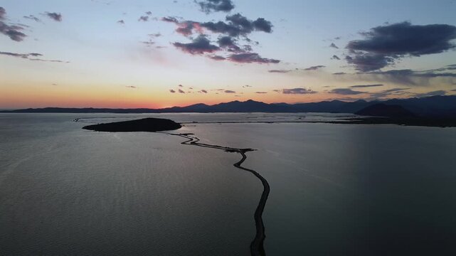 Stunning drone landscape of a colorful twilight sunset over the calm waters, islets and winding coastal pathways of Koronisia in Ambracian Gulf, Greece. High quality 4K cinematic b-roll.
