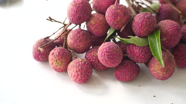 Fresh pink lychees clustered with natural branches and green leaves, showcasing a tropical fruit harvest with vibrant texture.
