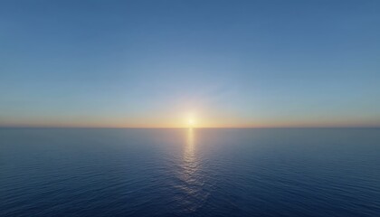 Obraz premium Ocean Sunrise Horizon: The sun rises over a vast, calm ocean, casting a golden path across the tranquil water under a clear blue sky, a symbol of new beginnings and serenity.