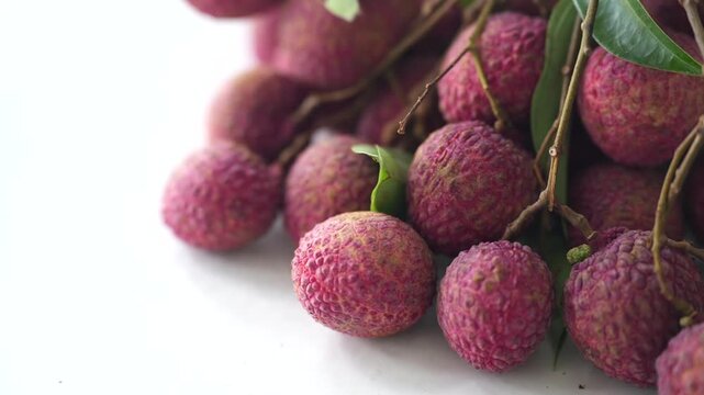 Fresh pink lychees clustered with natural branches and green leaves, showcasing a tropical fruit harvest with vibrant texture.