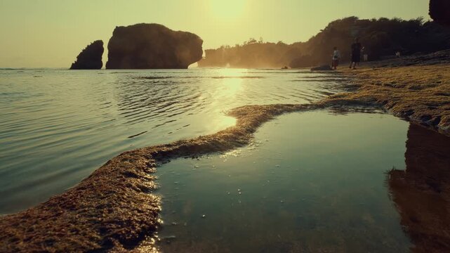 A cinematic low-angle view of a golden hour shoreline featuring jagged rock formations, calm reflecting tide pools, and a serene atmosphere on a tropical island coast.