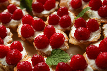 Gourmet raspberry tartlets with fresh red berries and creamy filling, featuring elegant moody lighting and mint leaf garnishes in a close-up composition. © Diana