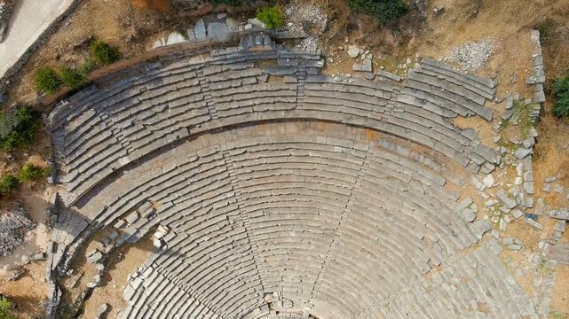 Delphi, Greece. Ancient stone theatre of Delphi, Drone footage over semicircular limestone seating tiers set into the Mount Parnassus hillside under bright summer sun. Drone footage, Departure of the