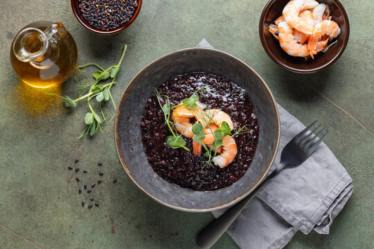 Black rice risotto with shrimps in ceramic bowl. Italian Cuisine. Top view
