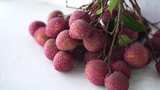 Fresh pink lychees clustered with natural branches and green leaves, showcasing a tropical fruit harvest with vibrant texture