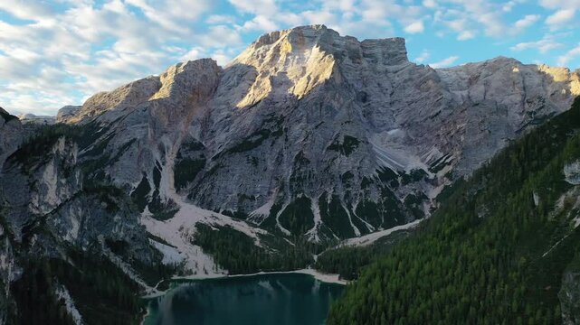 Stunning high-angle aerial drone shot of the emerald Lago di Braies lake in the Italian Dolomites. Features a thick green pine forest lining the water with the massive Croda del Becco peak above.