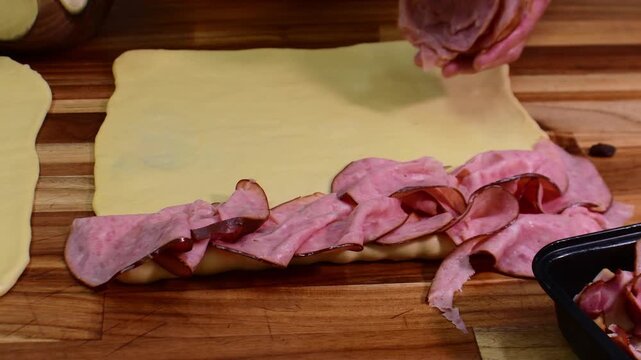 Chef layering sliced ham on fresh dough for Pan de Jamon preparation