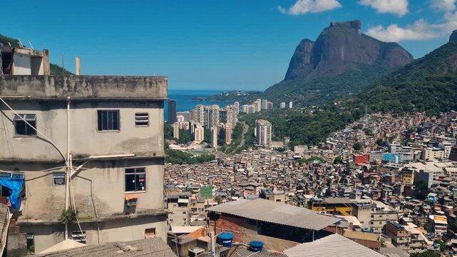 Panoramic view of Rocinha favela in Rio de Janeiro, Brazil, with tightly clustered hillside homes and modest architecture under bright sunshine, contrasting with modern high-rise buildings