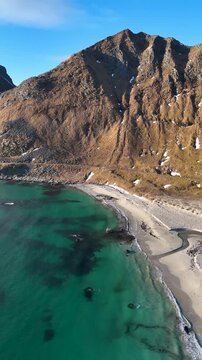 Marvelous Vertical Drone view of Turquoise Ocean Waves on Sandy Beach with Mountain Peak in Haukland Beach at sunset, Lofoten, Norway, 4K 60fs backwards aerial shot