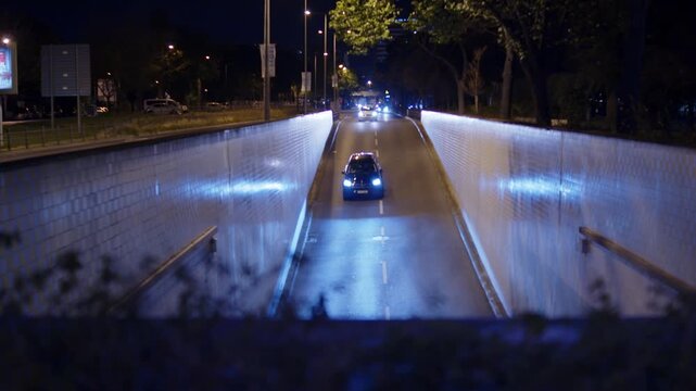 Cars driving into an illuminated concrete underpass tunnel at night. City traffic driving down a road tunnel at midnight. Late night streets filled with traffic. European late night traffic.