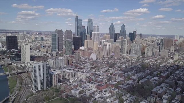 Aerial view of Philadelphia skyline with high rise buildings and urban architecture under clear blue sky with fluffy white clouds.