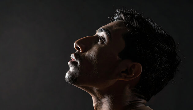 Man with wet hair and skin looking up with intense expression on dark background, strong side lighting
