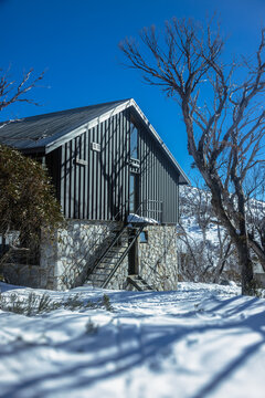 Modern alpine ski lodge with stone facade and dark corrugated steel siding in snowy Perisher Valley, Australia.