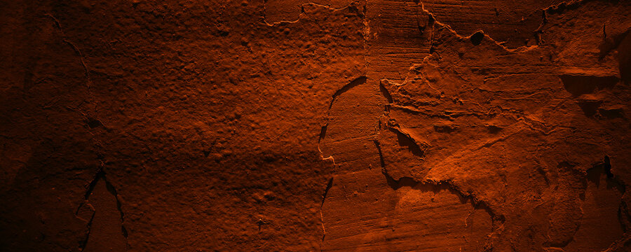 Roughtextured orange stone wall in dimly lit ancient cave, suitable for backgrounds in interior design or historical settings.