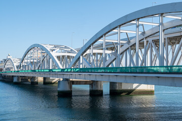 Fototapeta premium White Steel Arch Bridge with Teal Railing Spanning River Against Blue Sky