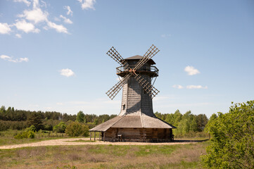 Fototapeta premium Rustic wooden windmill in countryside landscape with clear blue sky