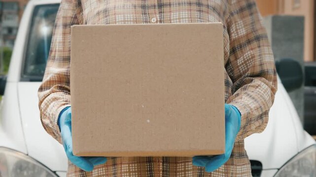 Delivery worker holding cardboard package in front of cargo van for contactless parcel drop off service during pandemic.