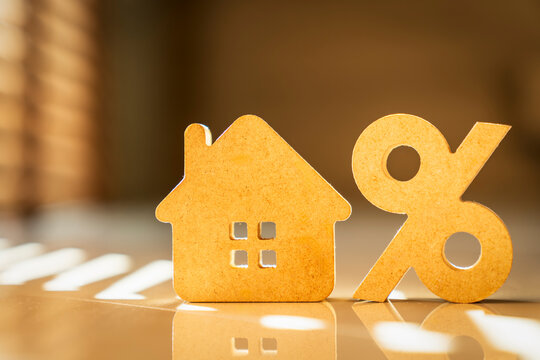 Wooden house model and percentage symbol on a desk with bright sunlight reflection. Concept of real estate mortgage, property loan interest rate, housing investment, and discount.