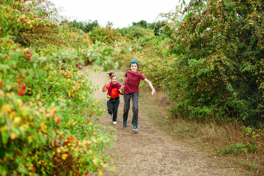 Happy siblings running through rural pathway during outdoor adventure