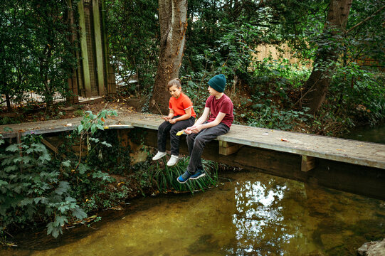 Teenager boy and child girl sitting together on the wooden bridge