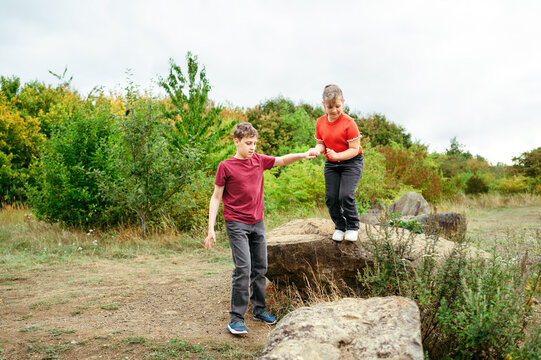Teenager boy helping younger sister step down from rock outdoors