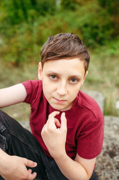 Thoughtful teenager boy looking at camera while sitting in park