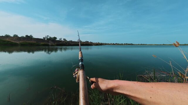 A person is fishing by the river while holding a fishing rod