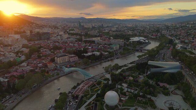 aerial of Tbilisi city skyline at sunset. Panoramic cityscape featuring the Kura River, historical Old Town architecture, and the modern Peace Bridge in Georgia, Caucasus