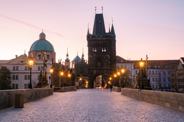 Obraz premium Early morning casts a warm glow on Charles Bridge in Prague, revealing its stunning Gothic architecture. Lanterns illuminate the cobblestone path, creating a magical atmosphere for early risers.