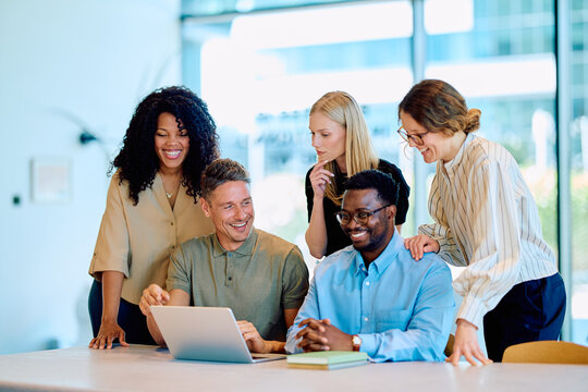Group of diverse business colleagues smiling and collaborating while looking at a laptop in a modern office