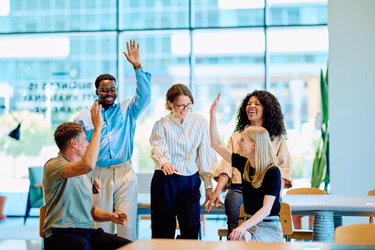 Diverse business team celebrating achievement, working together and giving high fives in a modern office environment